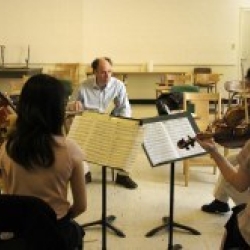 Students with instruments sitting in a semi-circle, with the professor in the center