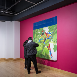 Two people looking at a large artwork mounted on a magenta wall. 